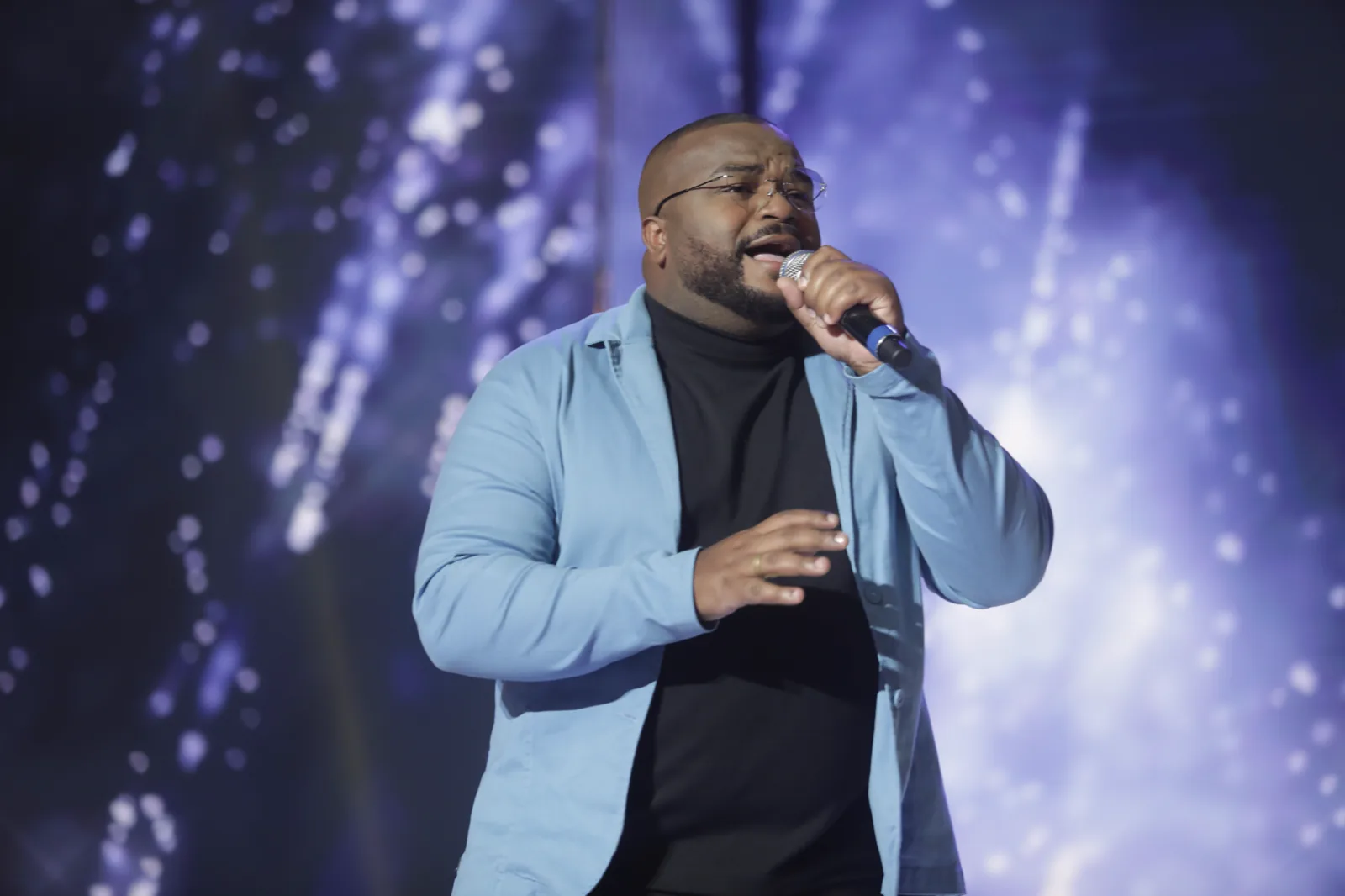 Kelvim canta com emoção sob luzes azuis, de blazer azul-claro